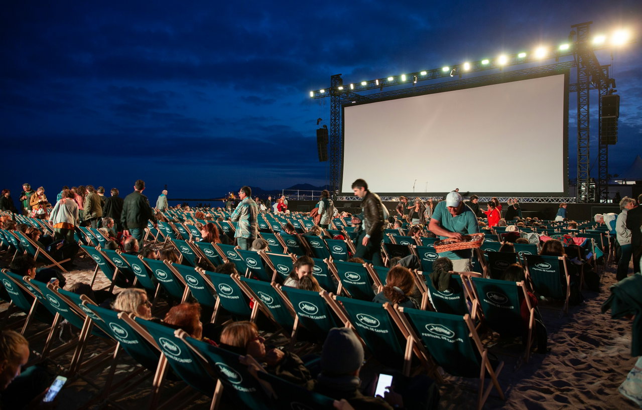 Open-Air-Kino am Strand zur blauen Stunde mit Liegestühlen, Publikum und großer Leinwand