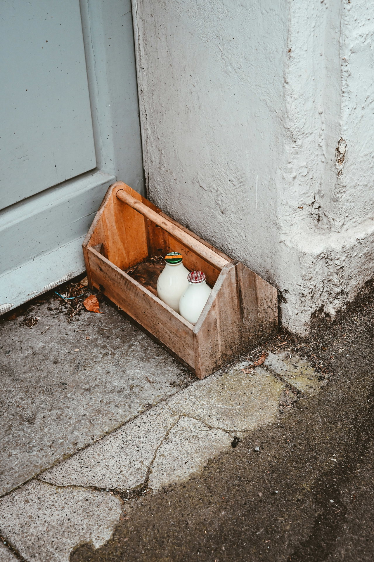 Kleine Holzkiste mit Zwiebeln steht neben einer Haustür auf dem Boden an der weißen Hauswand