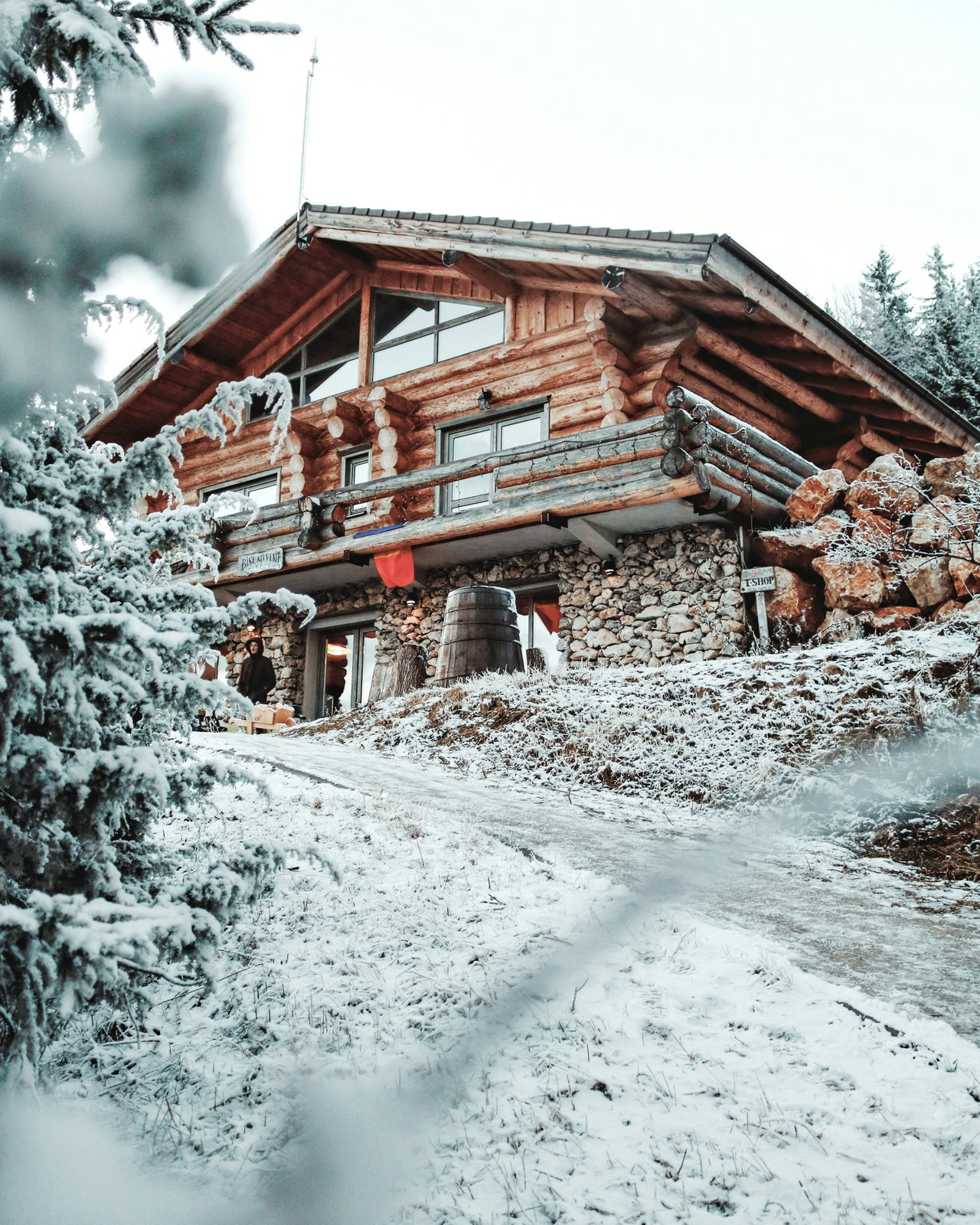 Großer Berggasthof aus dunklem Holz mit Balkonen, eingeschneit zwischen verschneiten Tannen am Hang