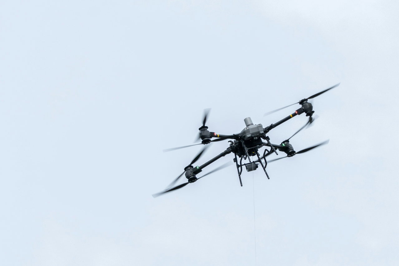 Inspektionsdrohne mit vier Rotoren im Flug vor hellblauem Himmel