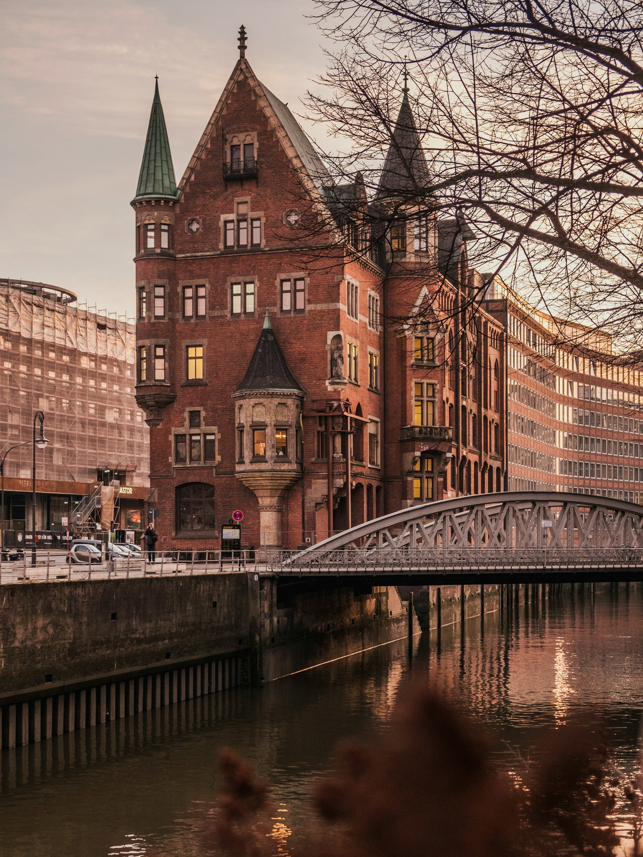 Backsteingebäude mit Türmchen an einem Kanal, davor eine eiserne Brücke