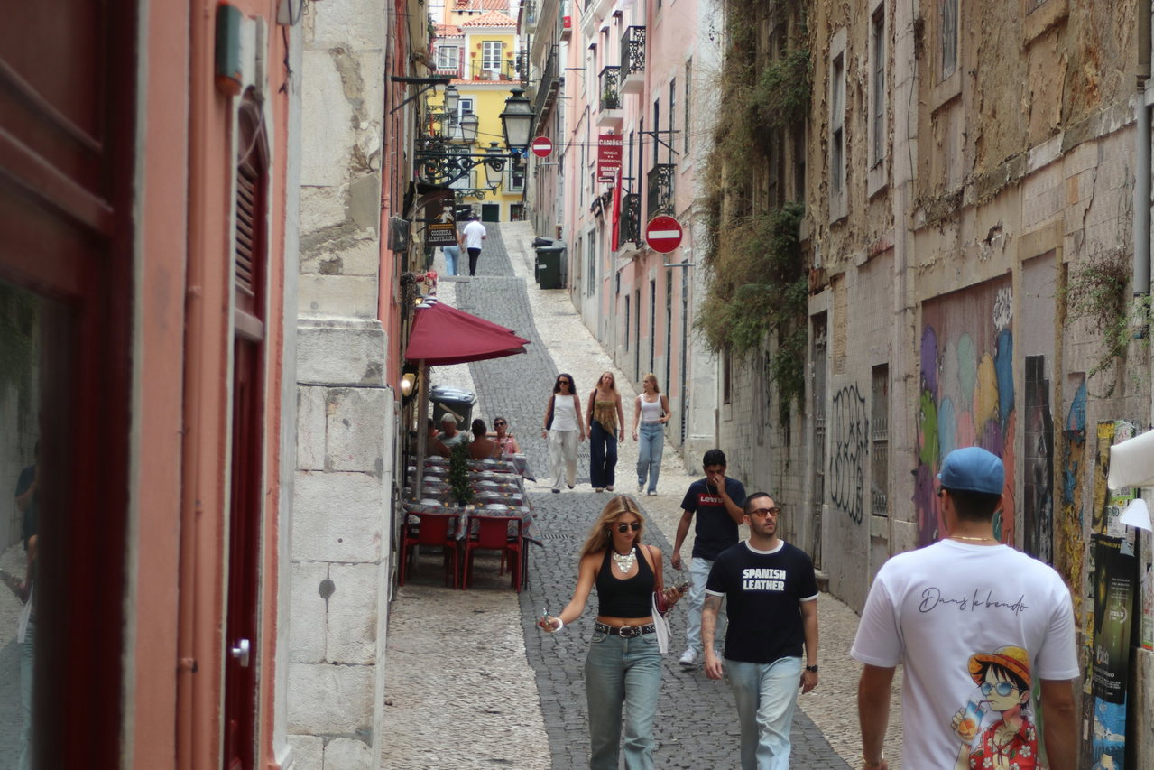 Junge Leute gehen durch eine steile Altstadtgasse in Lissabon mit Pflaster, Graffiti und bunten Fassaden