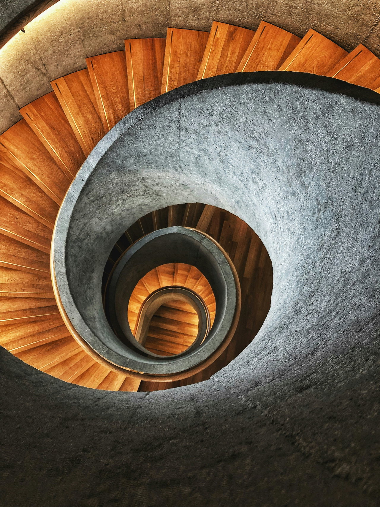 Wendeltreppe mit Holzstufen und Betonwand, von oben in die Spirale fotografiert