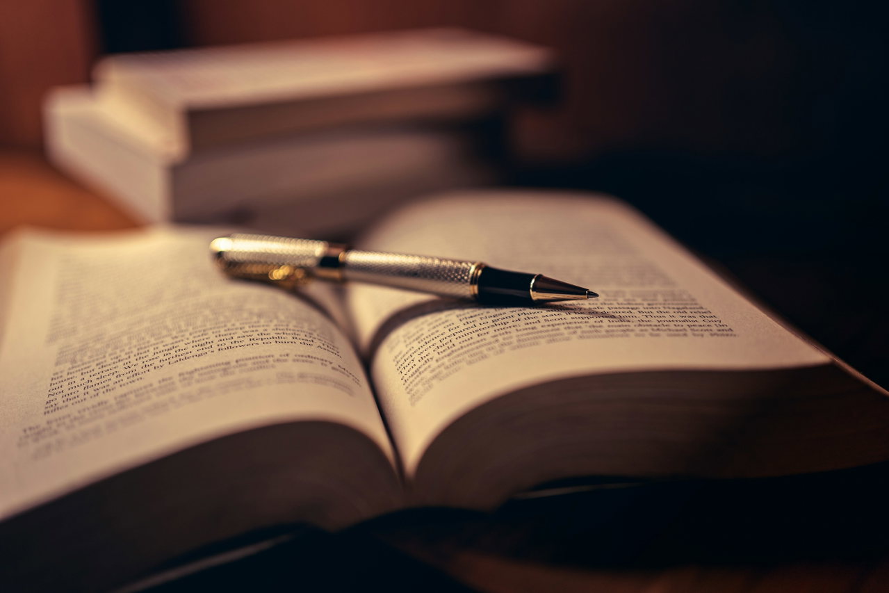 Ein Füllfederhalter liegt auf einem aufgeschlagenen Gesetzbuch, daneben weitere Bücher im warmen Licht