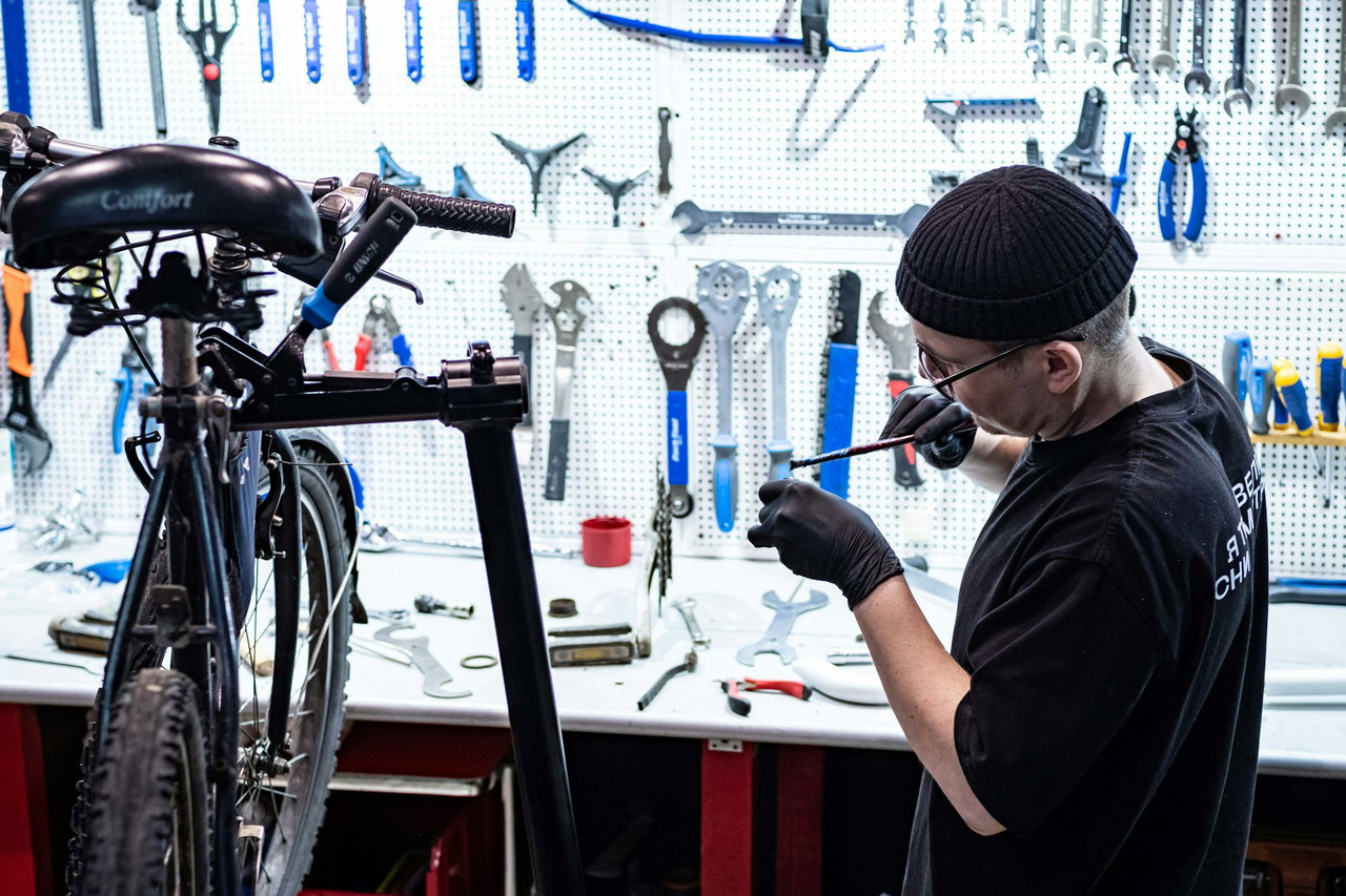 Mechaniker mit Mütze und Brille arbeitet am Montageständer vor einer Lochwand voller Werkzeug