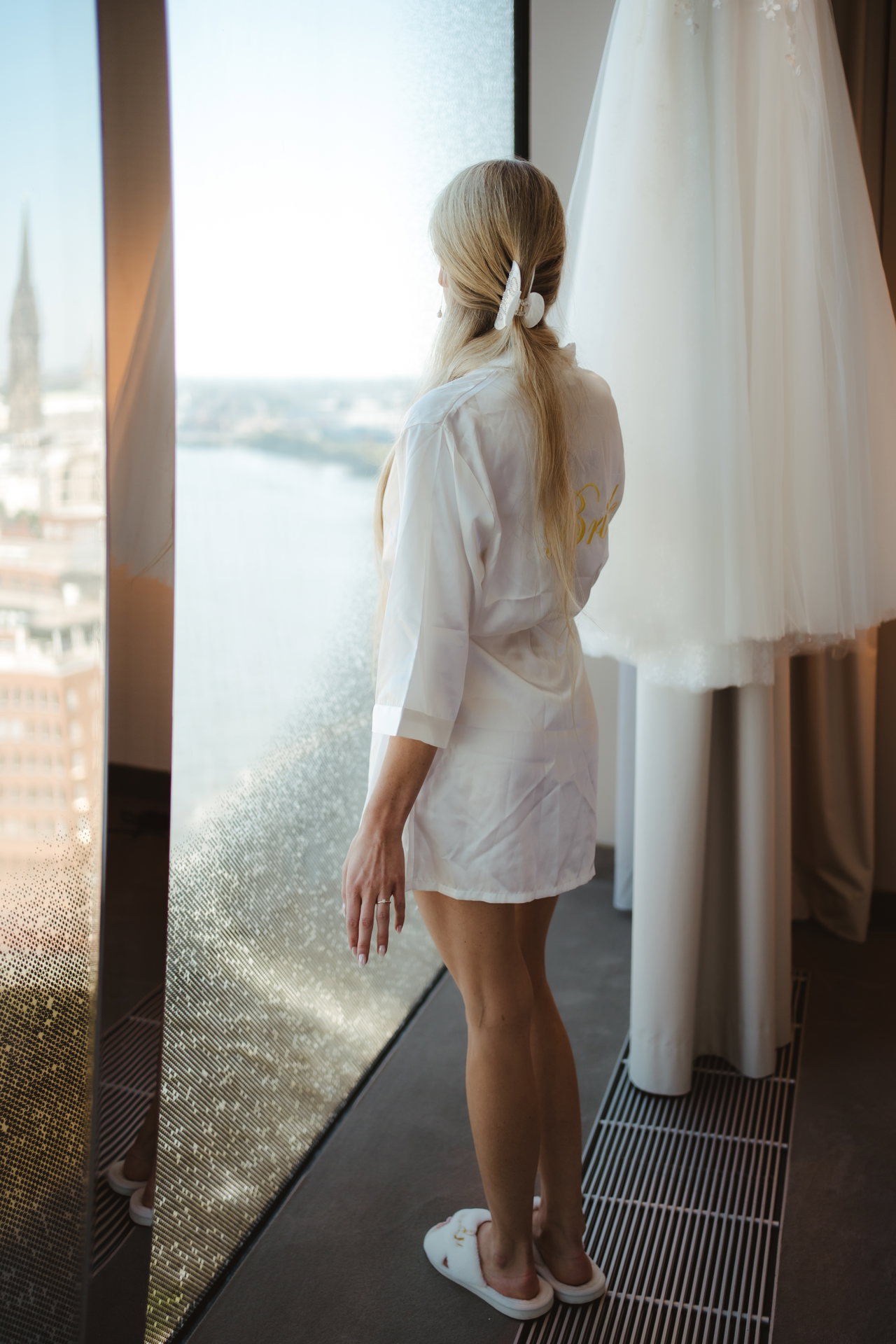 Elain im weißen Morgenmantel am Fenster neben dem Brautkleid