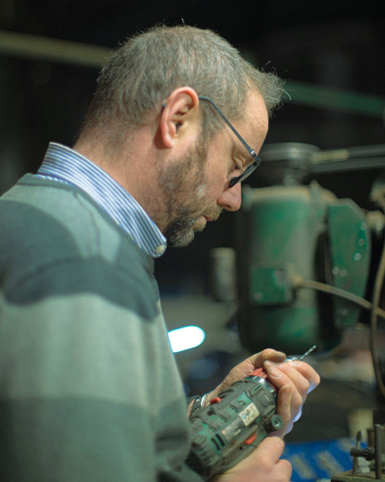 Erfahrener Handwerker mit Brille prüft in der Werkstatt eine Bohrmaschine.