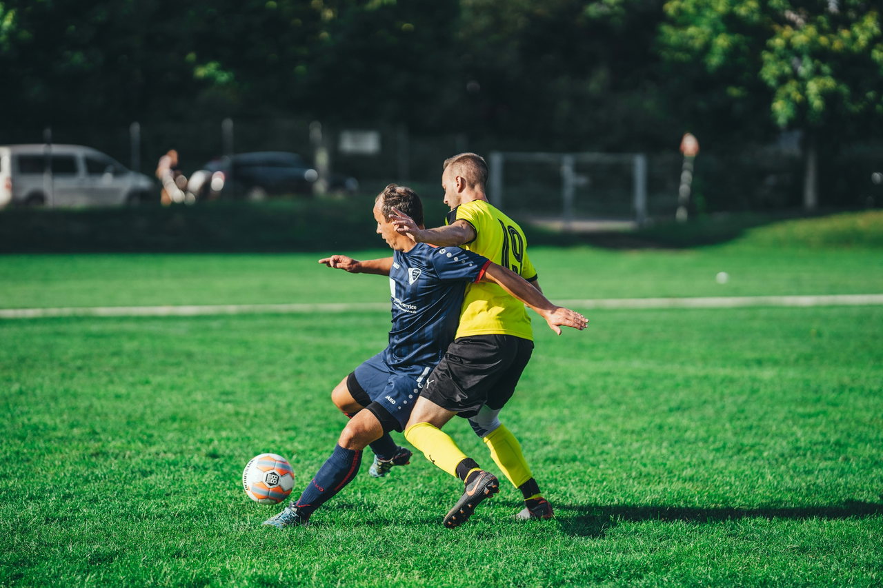 Zwei Spieler im Zweikampf um den Ball auf einem grünen Rasenplatz, einer in Blau, einer in Neongelb