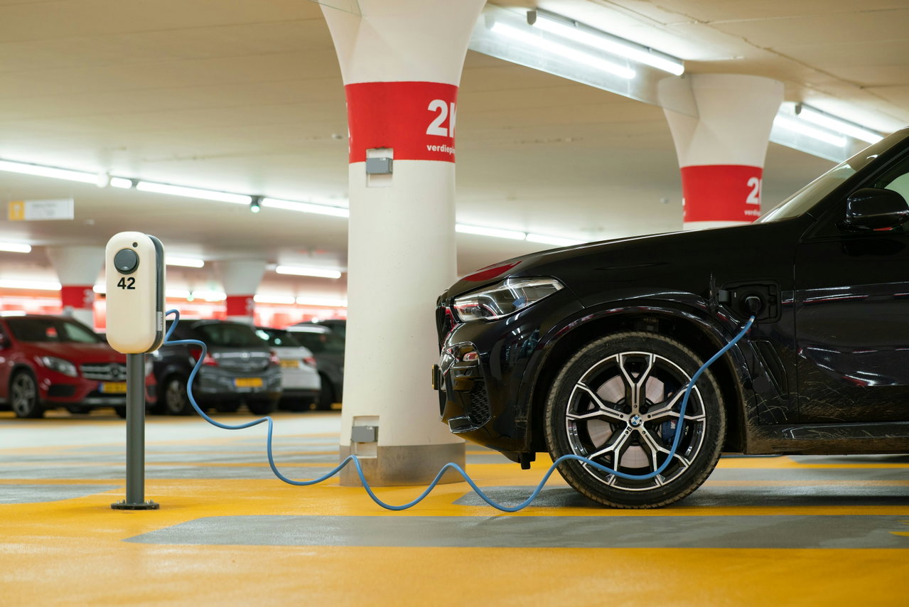 Electric car charging at a charging point in a car park with a yellow floor and red-and-white pillars