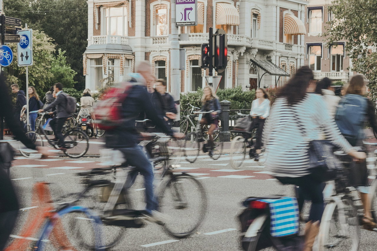 Viele Pendlerinnen und Pendler radeln im Berufsverkehr über eine Kreuzung, die Bewegung verwischt ihre Umrisse
