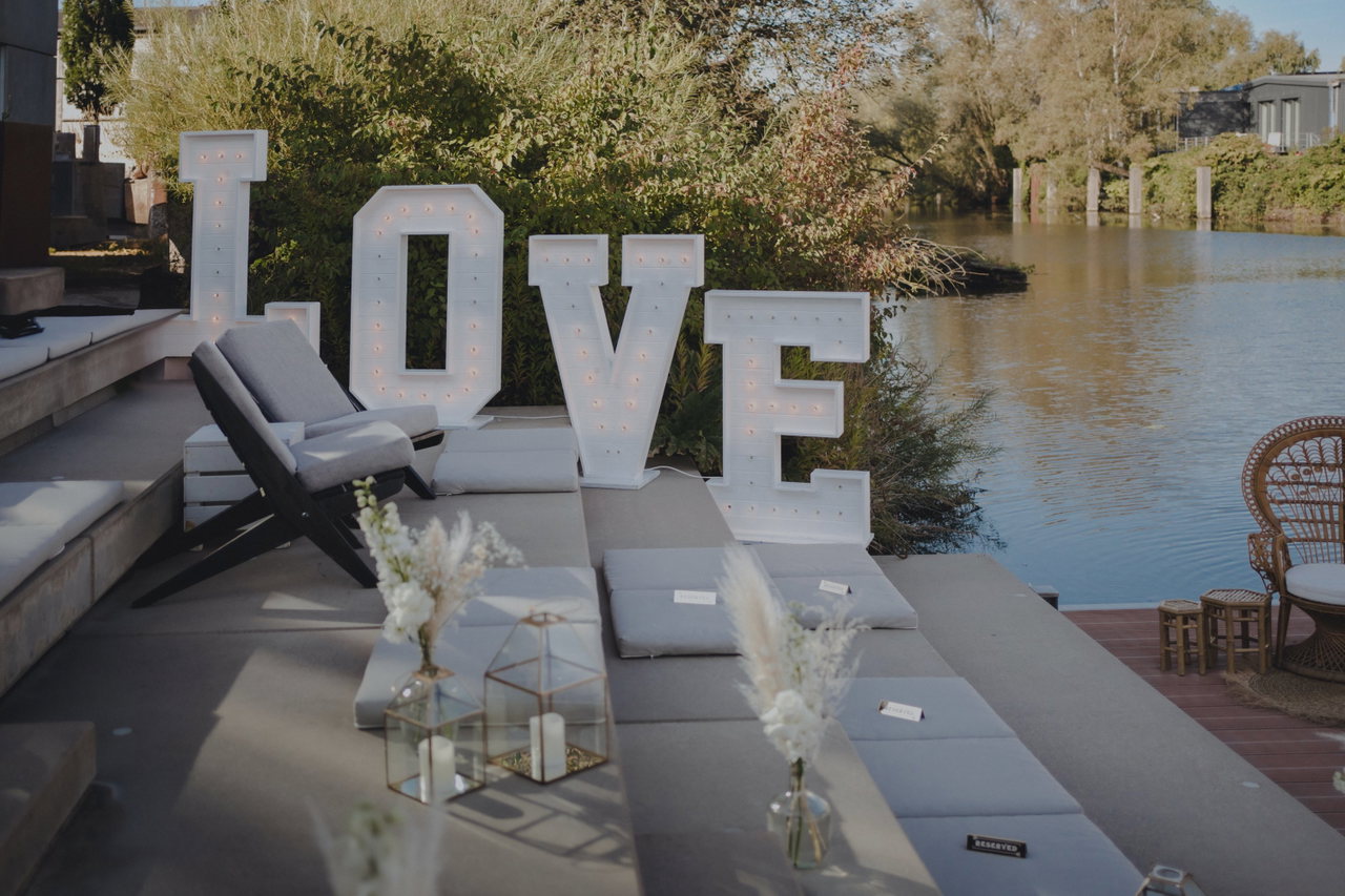 LOVE-Leuchtbuchstaben am Wasser, davor Lounge-Möbel