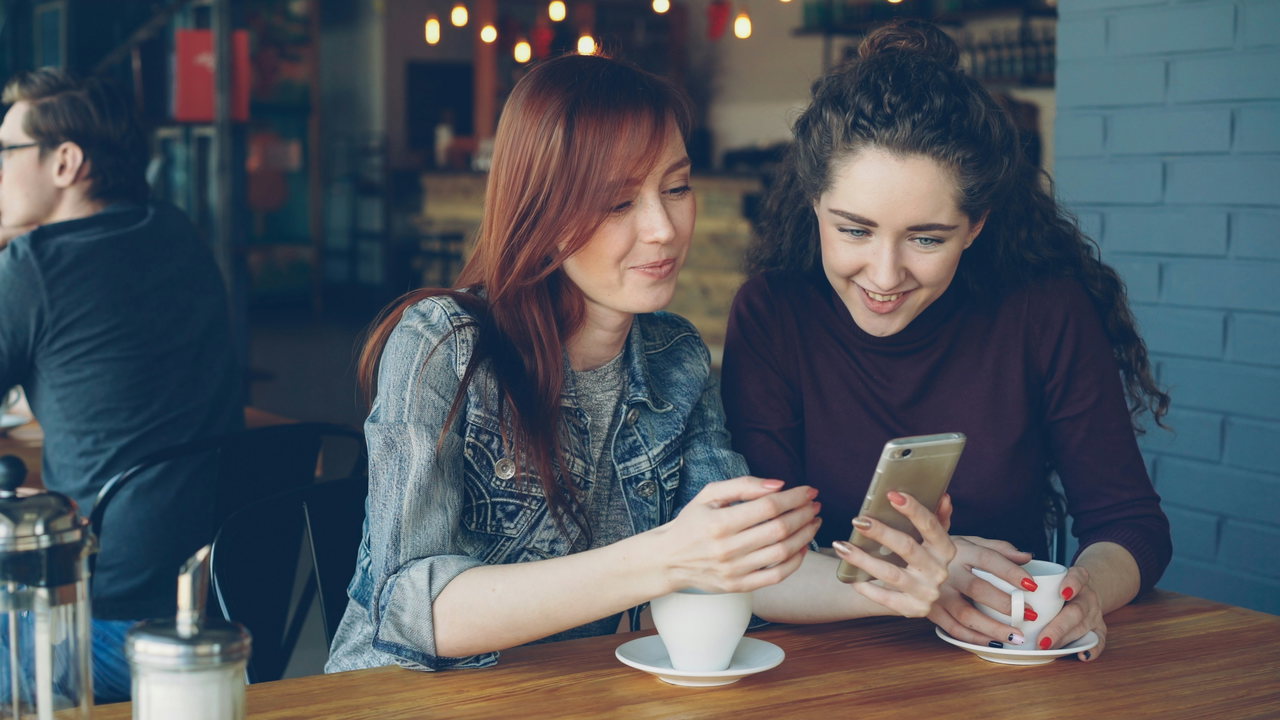 Zwei Frauen lesen im Café Nachrichten auf dem Smartphone