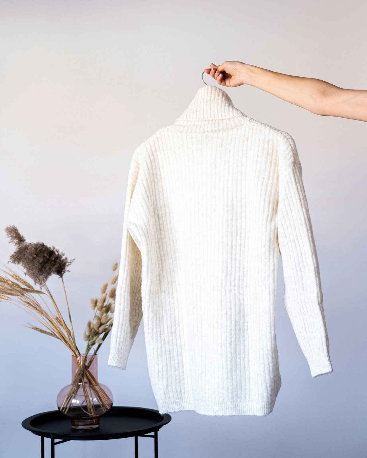Weißer feiner Rollkragenpullover, von einer Hand am Bügel gehalten, vor hellem Hintergrund