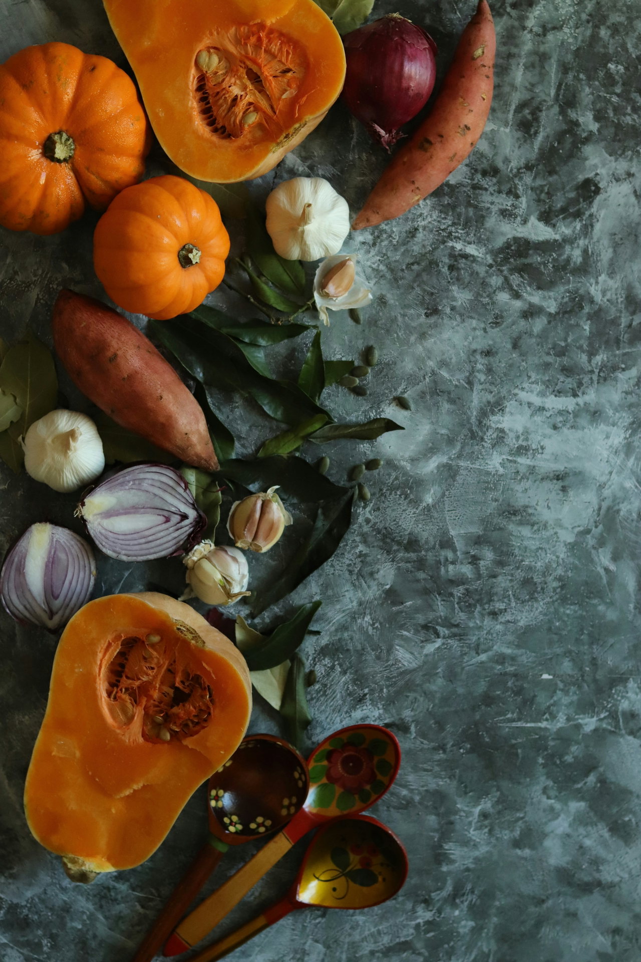 Zutaten für Herbstgerichte: Kürbisse, Zwiebeln, Knoblauch und Süßkartoffeln auf grünlichem Stein