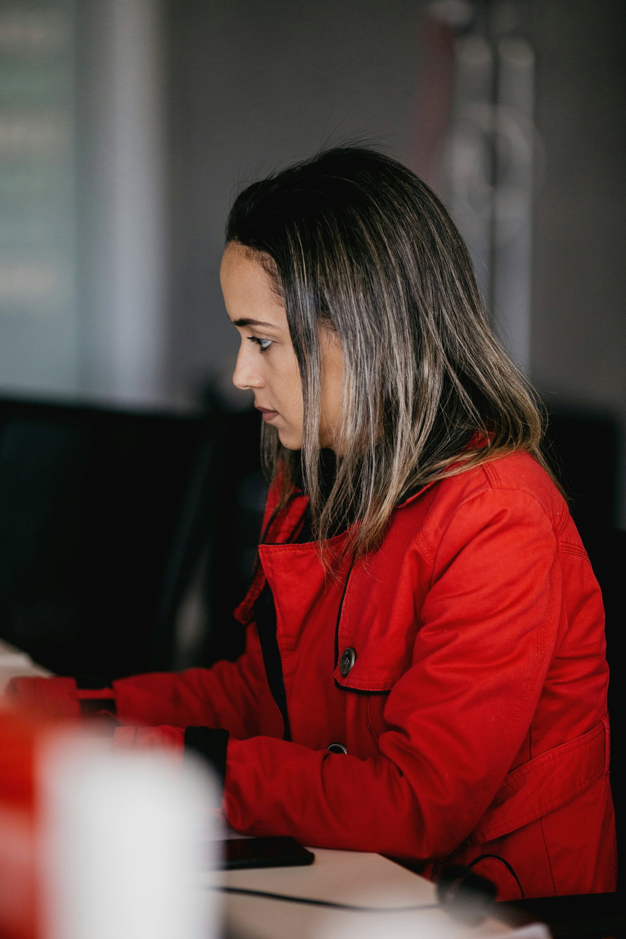 Frau in roter Jacke arbeitet konzentriert an einem Computerarbeitsplatz.