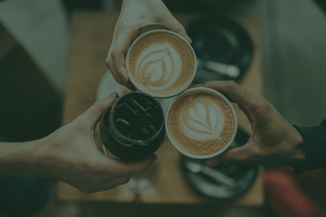 Three hands clink their coffee cups together
