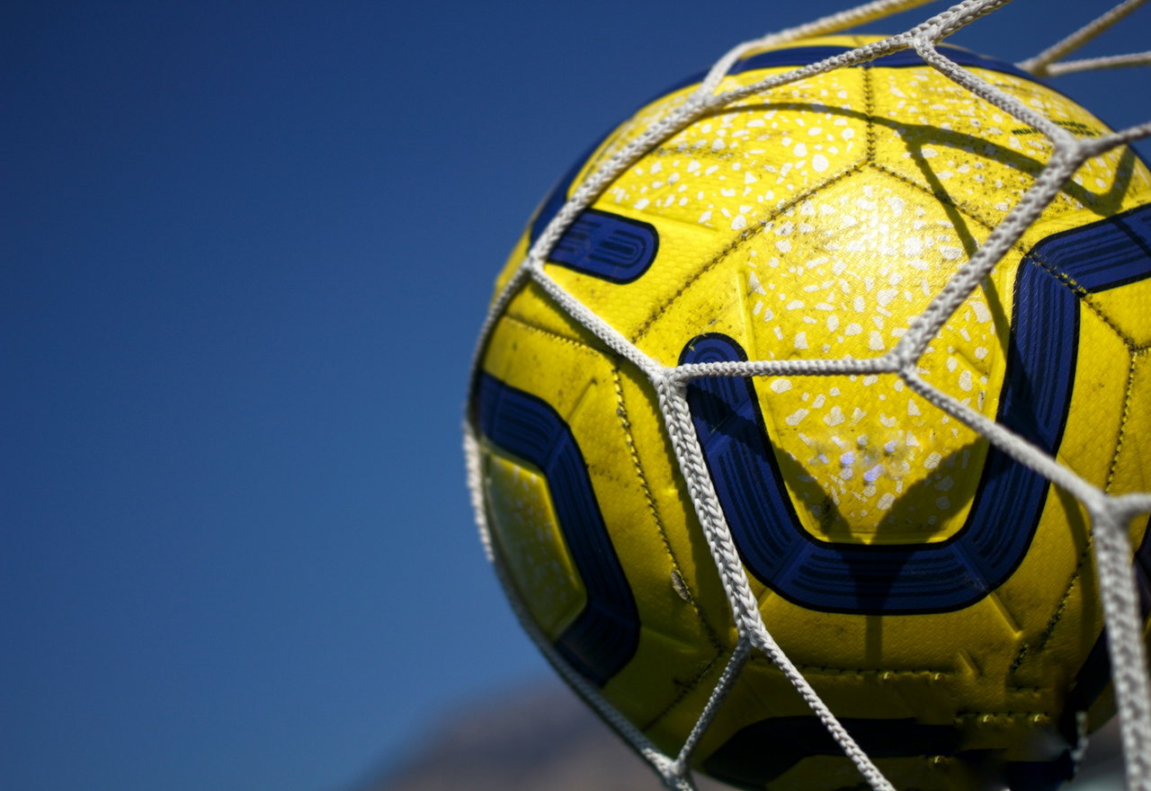 Gelb-blauer Fußball verfängt sich im weißen Tornetz vor tiefblauem Himmel