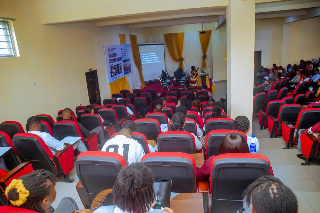 Full rows of lecture-hall seats in red, students seen from behind during a lecture with a presentation