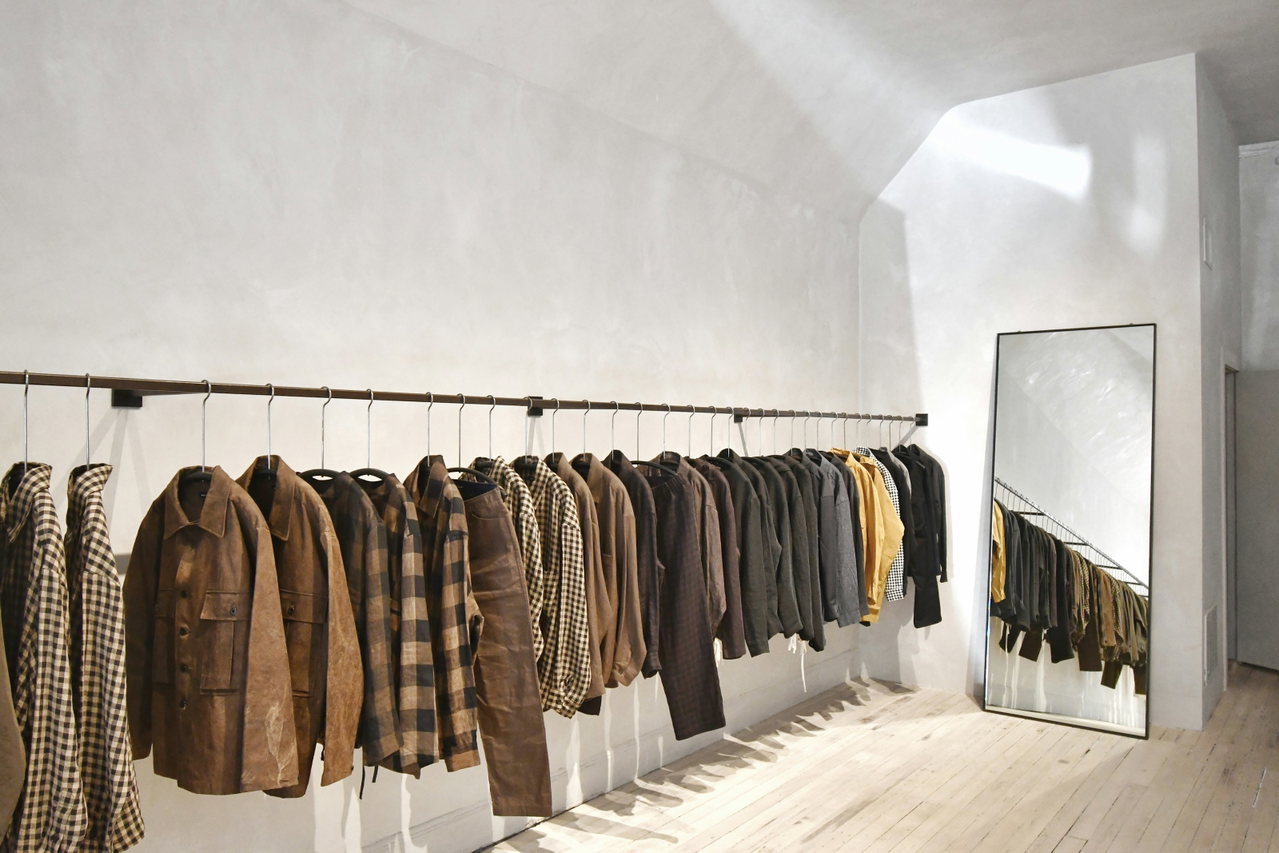 Heller, minimalistischer Modeladen mit langer Kleiderstange voller brauner Jacken und Mäntel, Spiegel an der Wand