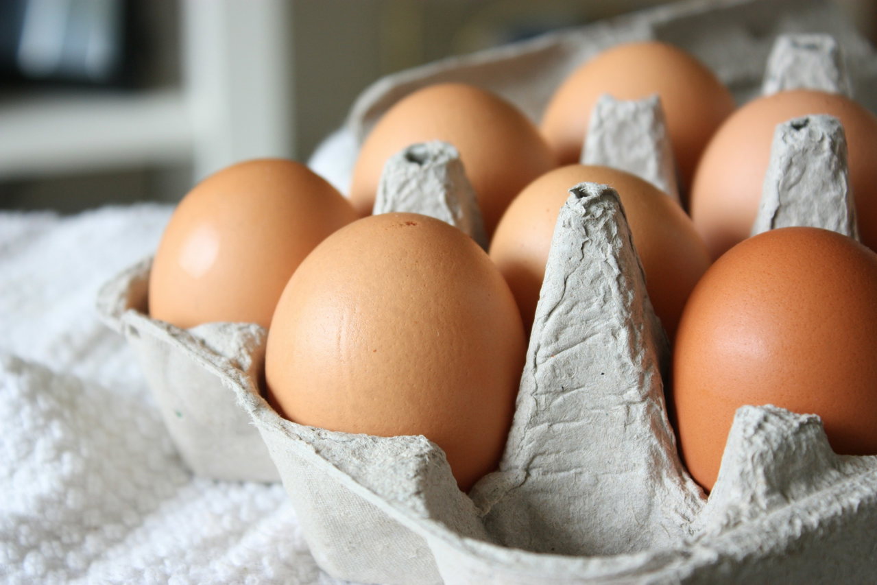 Frische braune Eier in einem Eierkarton auf einem weißen Tuch, Nahaufnahme