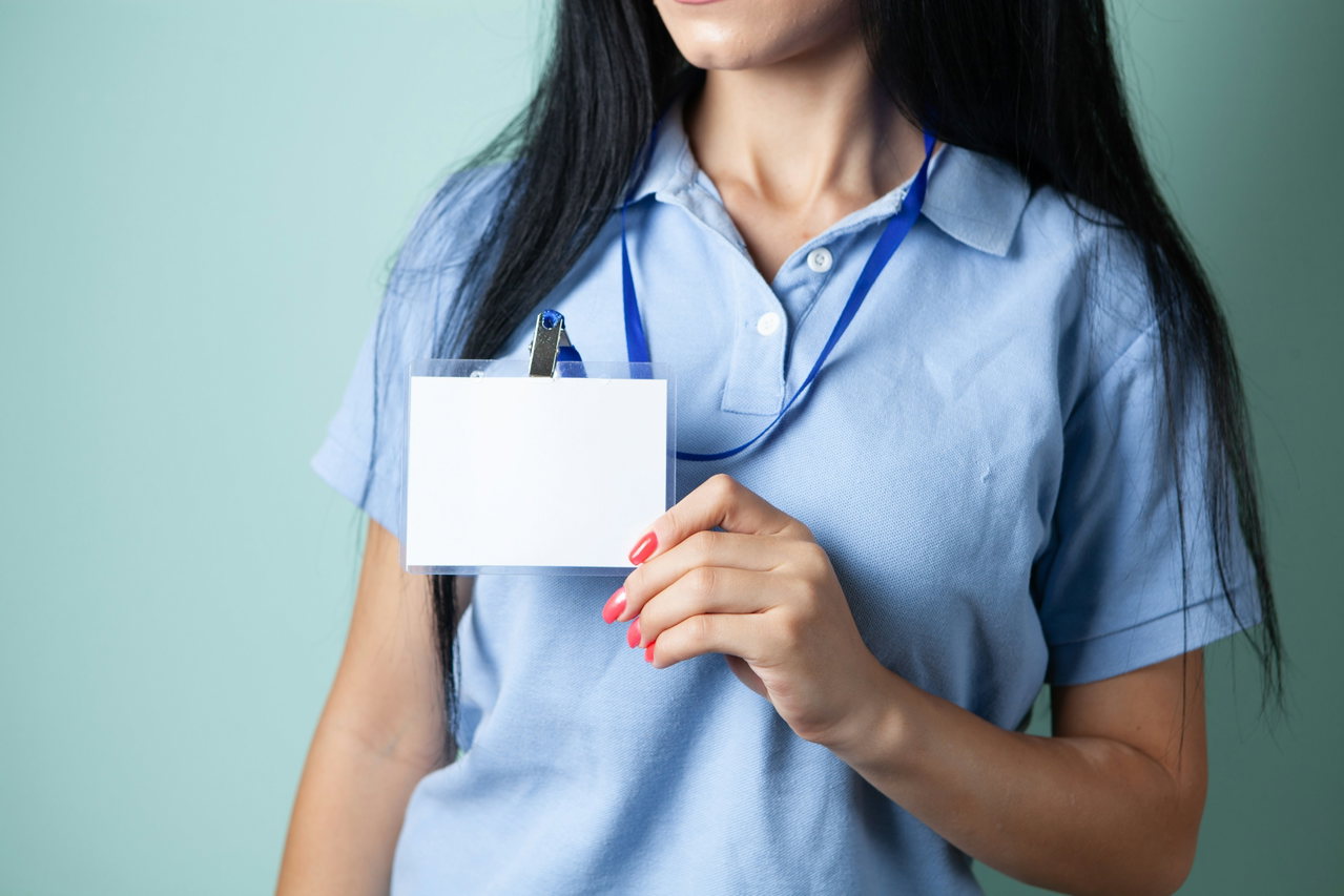 Person in a light blue polo shirt holding an empty visitor badge on a blue lanyard