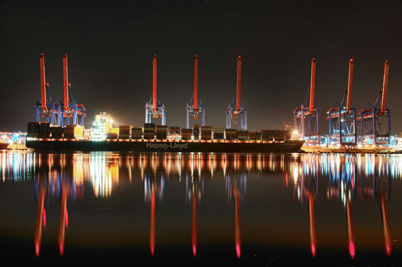 Containerterminal bei Nacht, die Lichter spiegeln sich im Wasser