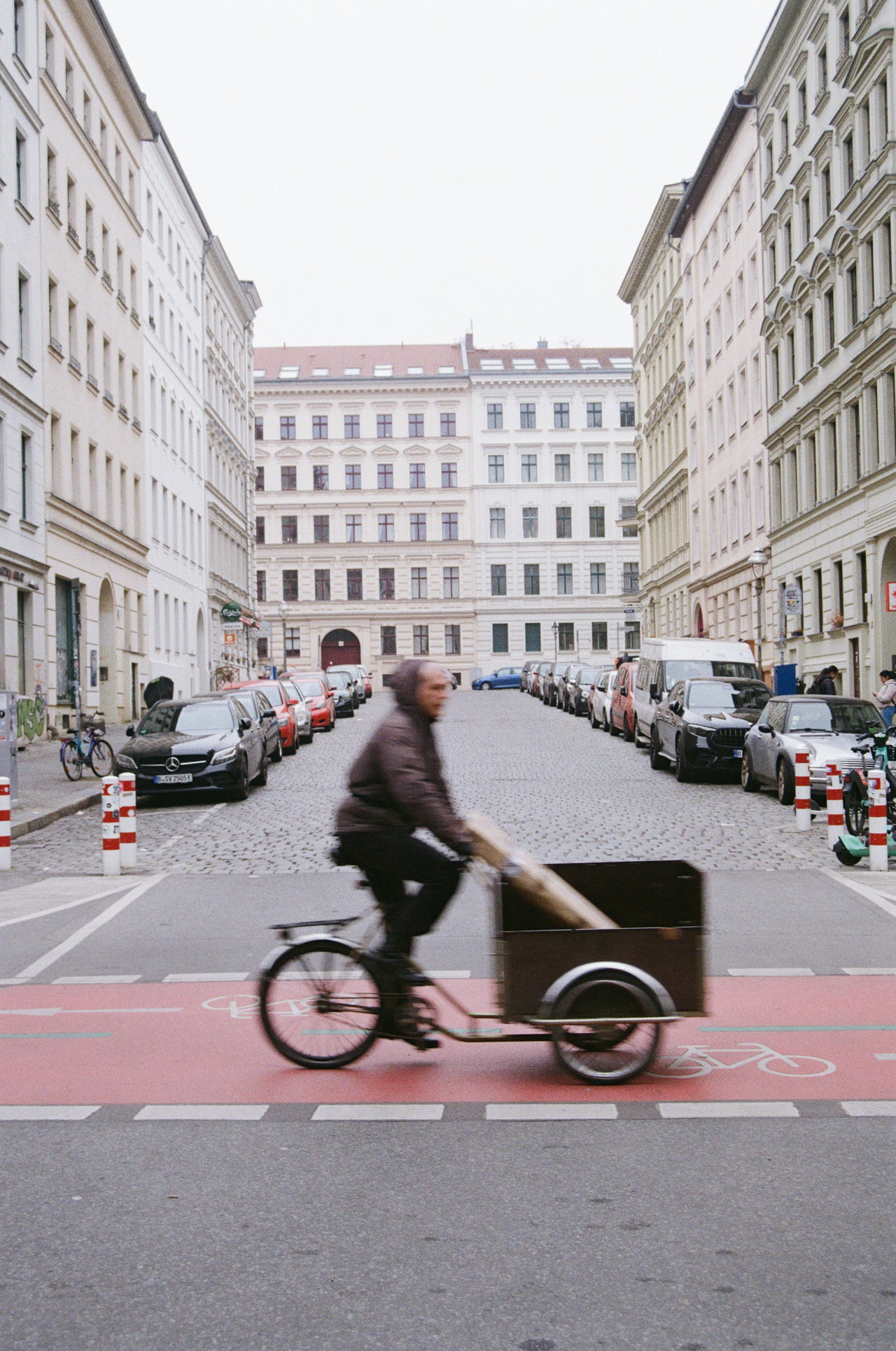 Mann fährt ein Lastenrad mit Holzkiste über einen roten Radweg in einer Straße mit Altbauten