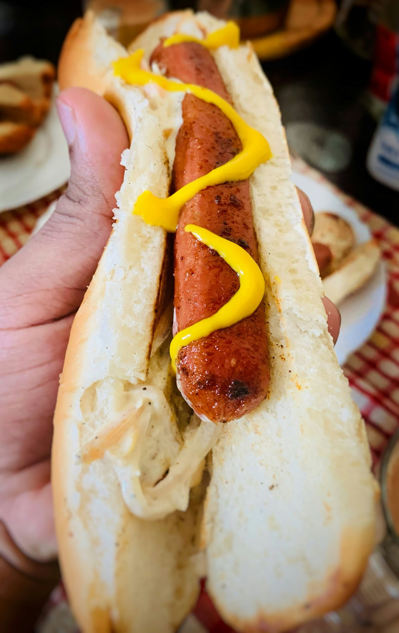 Hand hält ein Brötchen mit Bratwurst und gelbem Senf, Stadionimbiss in Nahaufnahme