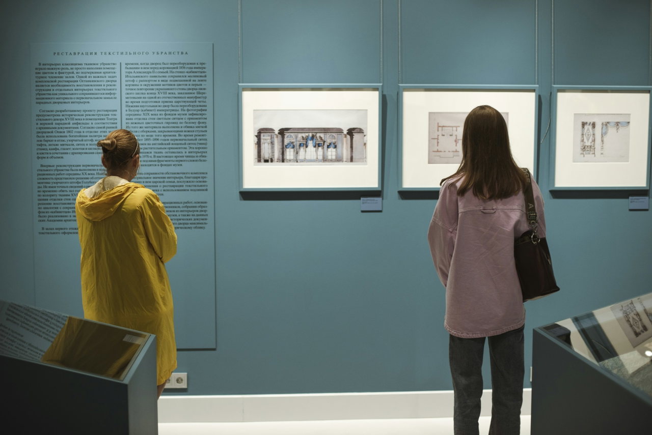 Zwei Besucherinnen betrachten gerahmte Zeichnungen an einer petrolfarbenen Museumswand