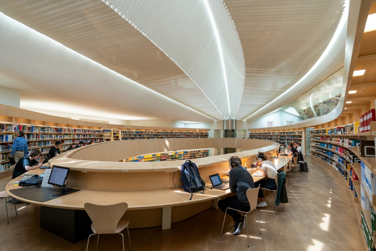 Helles, modernes Lernzentrum mit geschwungener Decke, Bücherregalen und Arbeitsplätzen mit Laptops
