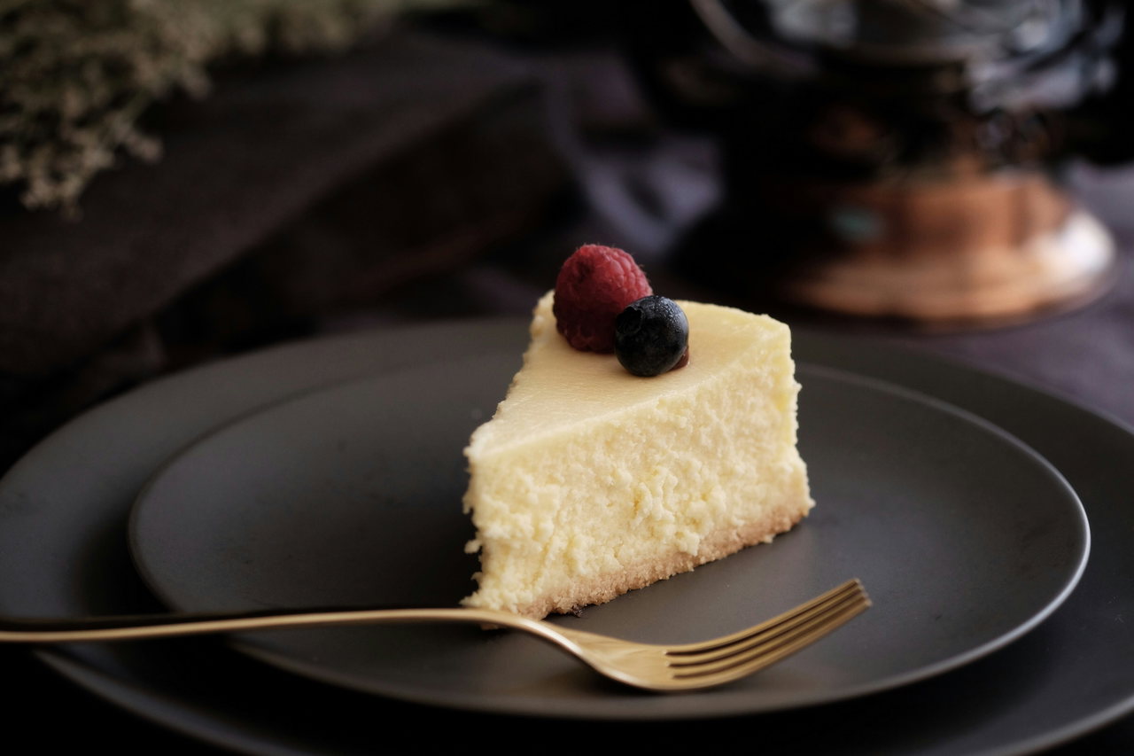 Stück Cheesecake mit Beeren auf dunklem Teller