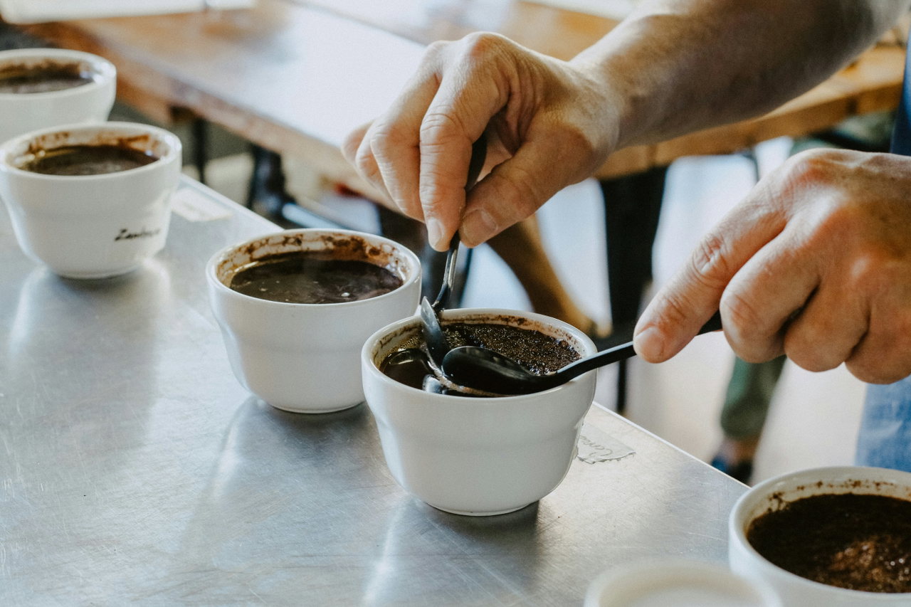 Hände mit Löffeln über Tassen bei einem Cupping