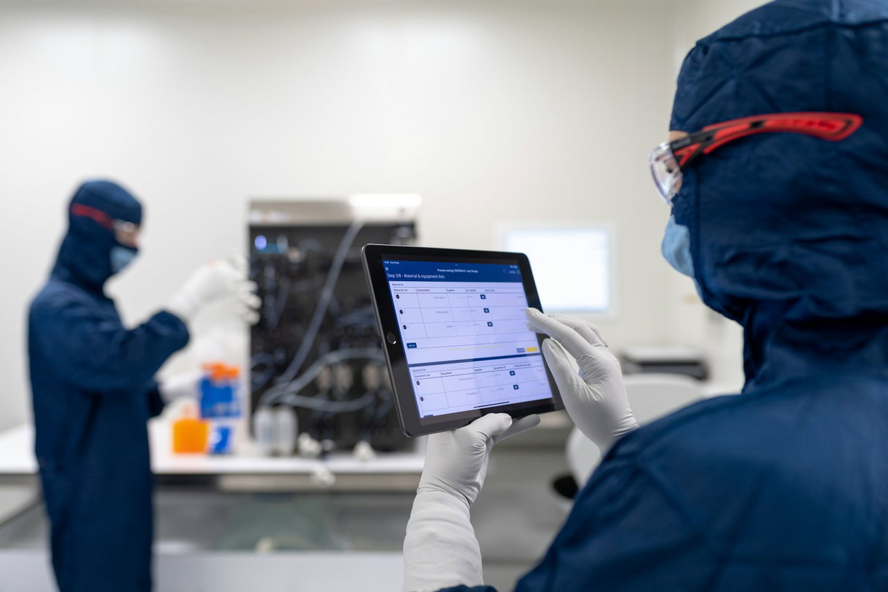 Techniker in Schutzanzug prüft mit einem Tablet die Messwerte einer Anlage im Hintergrund