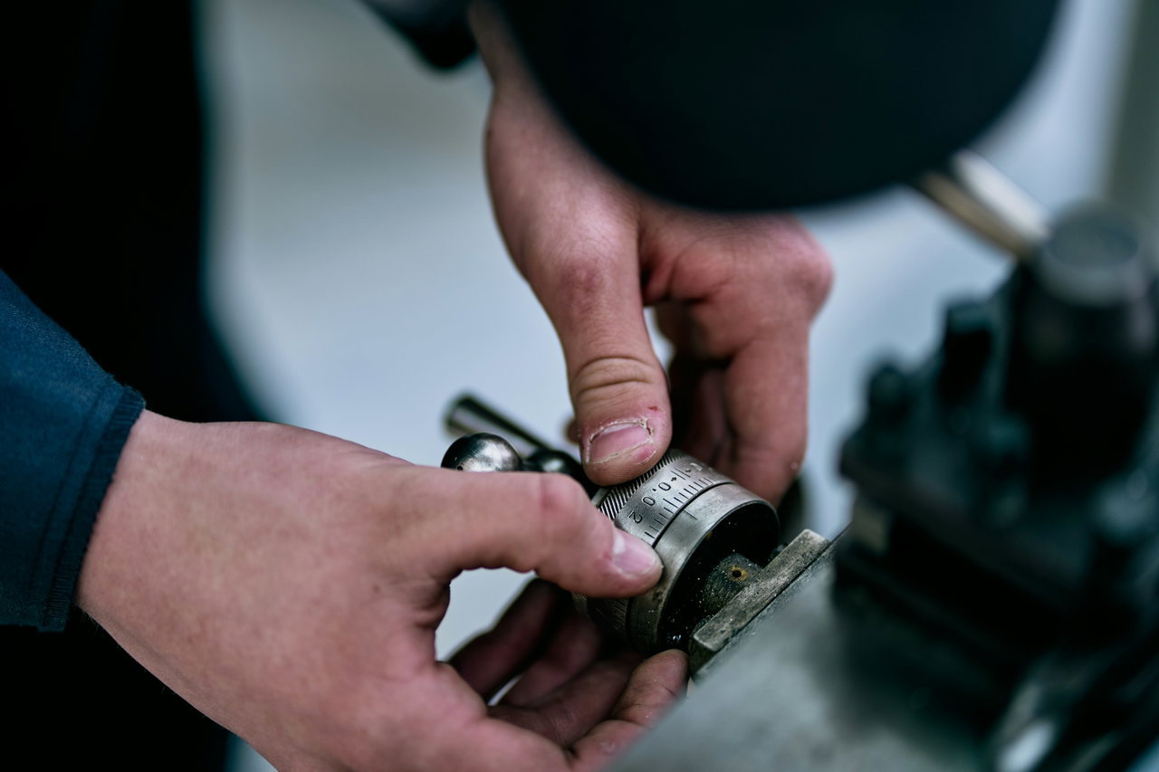 Hände halten ein metallisches Bauteil, das an einer Maschine geprüft und instand gesetzt wird