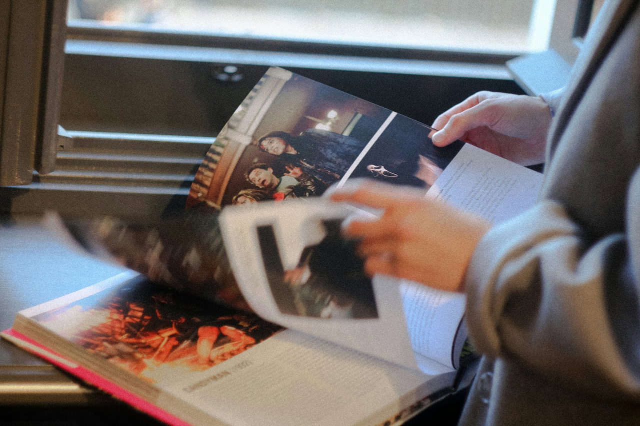 Hände halten ein gedrucktes Magazin neben einem Tablet am Fenster