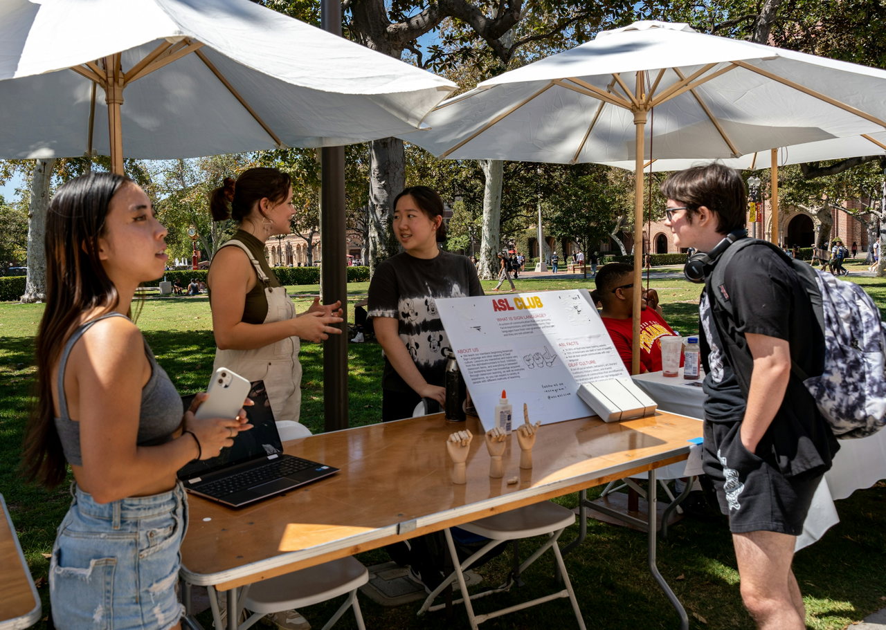 Visitors and students talking at an information stand under parasols on Open Day