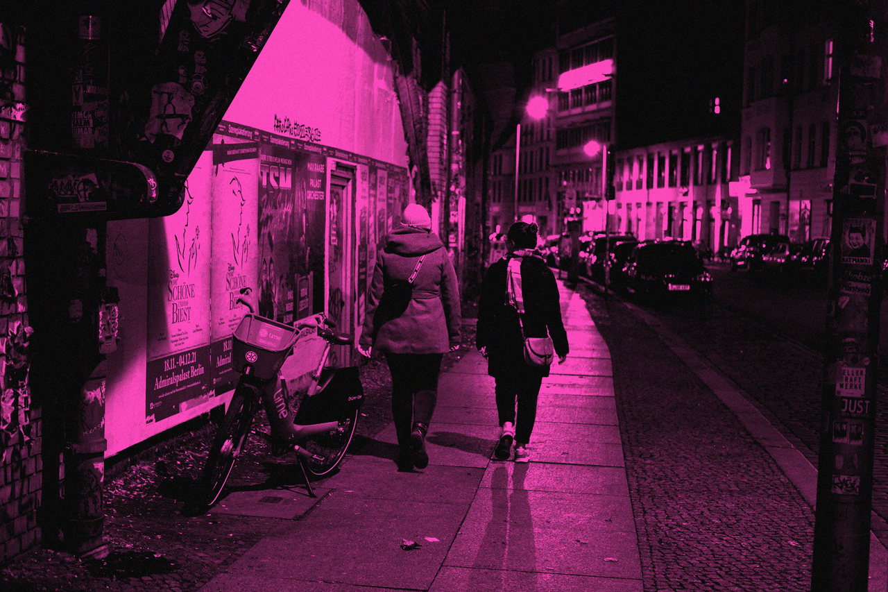 Weserstraße bei Nacht: zwei Menschen auf dem Gehweg neben einem abgestellten Fahrrad, Schwarzweiß mit Magenta-Duplex