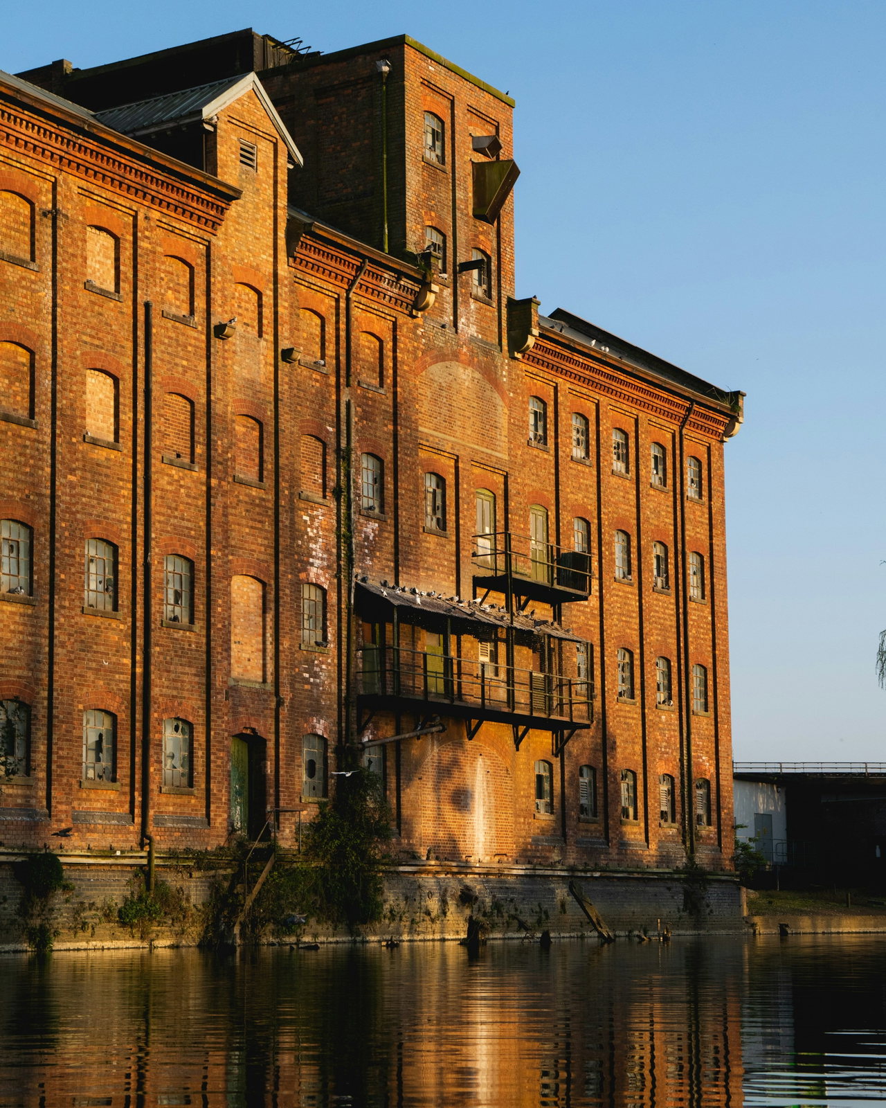 Alter Speicherbau aus rotem Backstein im warmen Abendlicht, dessen Fassade sich im ruhigen Kanal spiegelt.