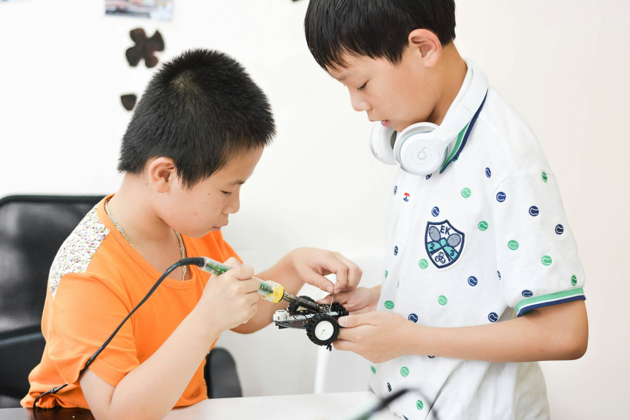 Zwei Jugendliche löten und basteln gemeinsam an einem kleinen elektronischen Modell, Berufsorientierung zum Ausprobieren