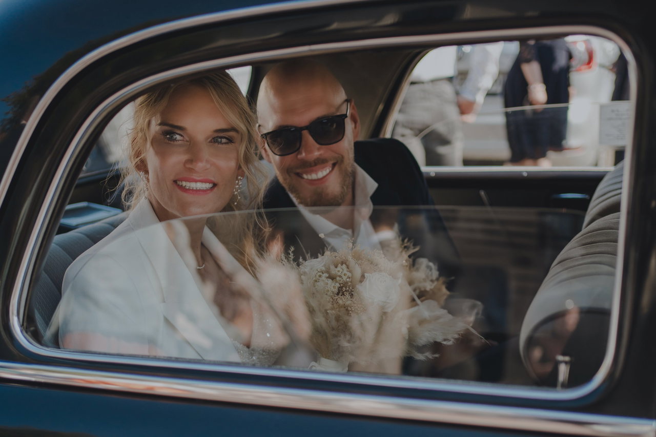 Elain und Marcel lachen aus dem Fenster eines Oldtimers