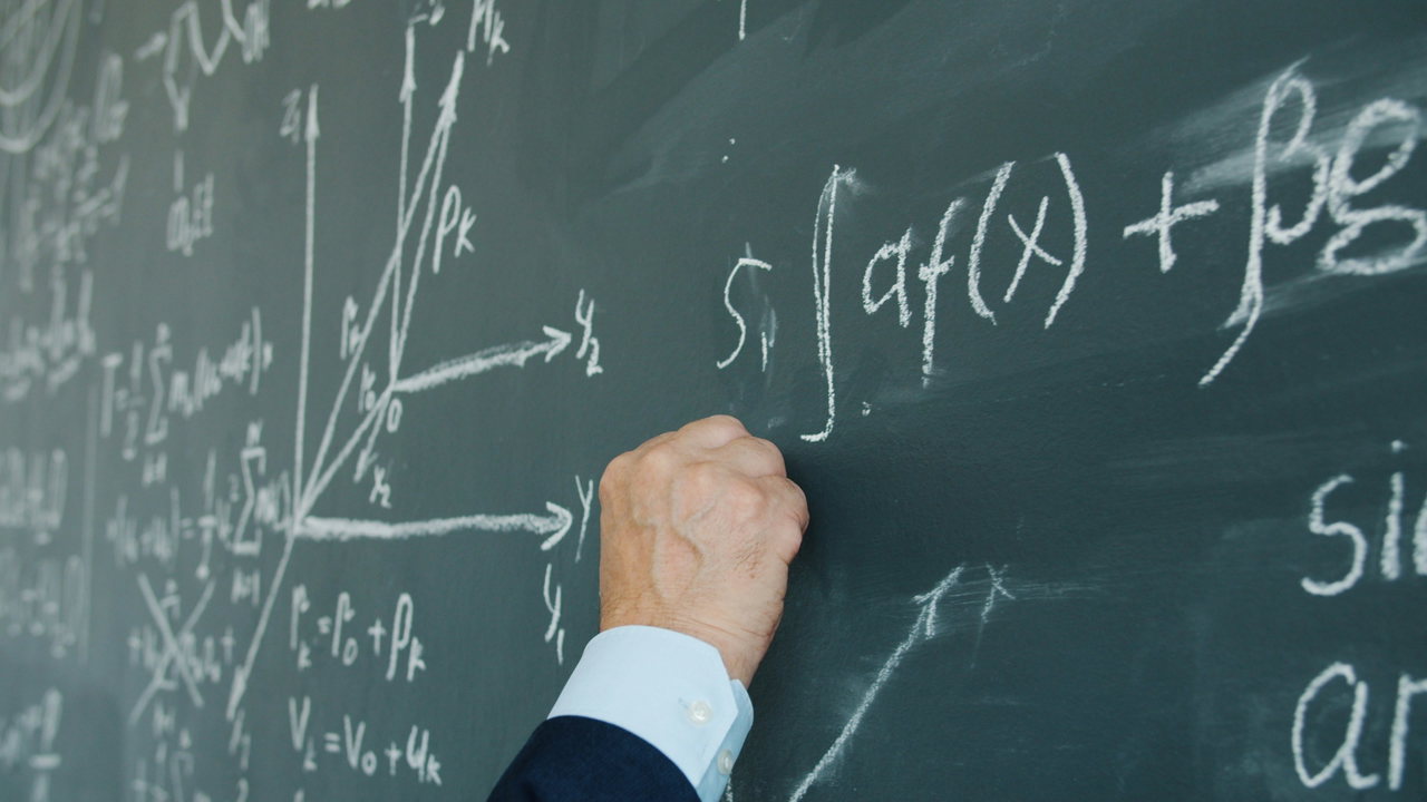 Nahaufnahme einer Hand, die mathematische Formeln und Koordinatensystem mit Kreide an eine grüne Tafel schreibt