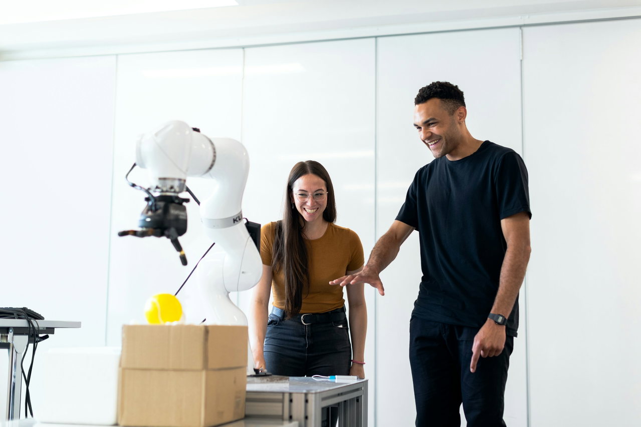Zwei Fachleute lächeln und stehen neben einem weißen kollaborativen Roboterarm mit Greifer