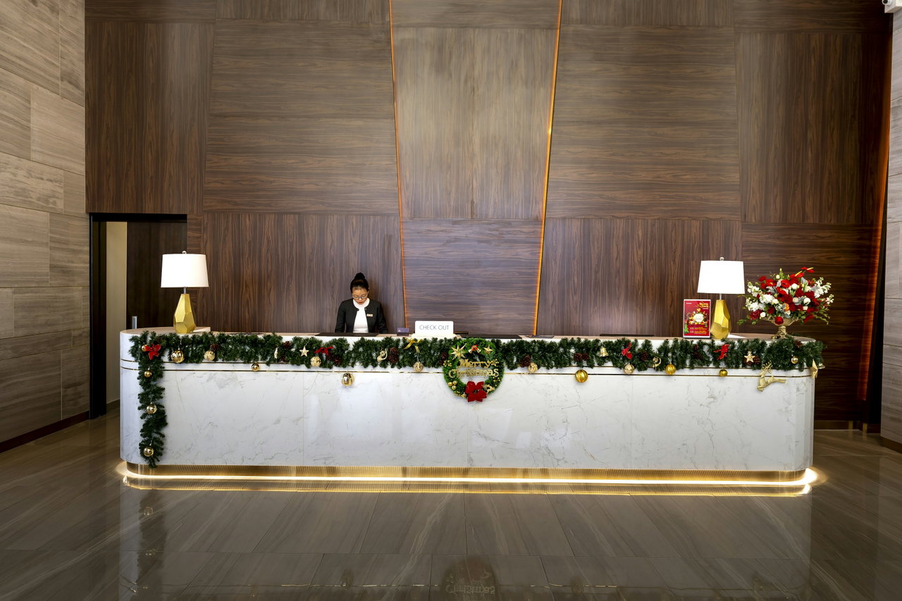 Lange Holzrezeption mit Tannengirlande und Lampen in einer Hotelhalle, eine Mitarbeiterin wartet dahinter
