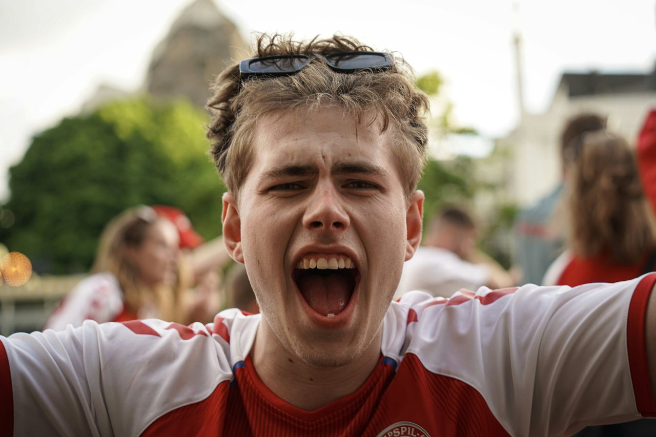 Junger Fan in rot-weißem Trikot schreit begeistert vor Freude, die Arme weit ausgebreitet