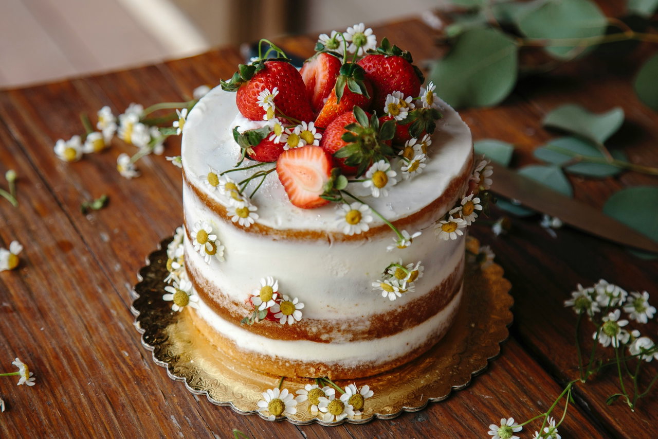 Naked Cake mit frischen Erdbeeren und Gänseblümchen auf einem Holztisch