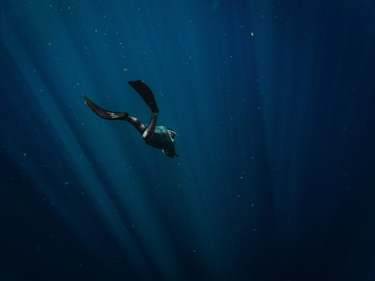 Ein Freitaucher mit langen Flossen gleitet durch Sonnenstrahlen im tiefblauen Wasser