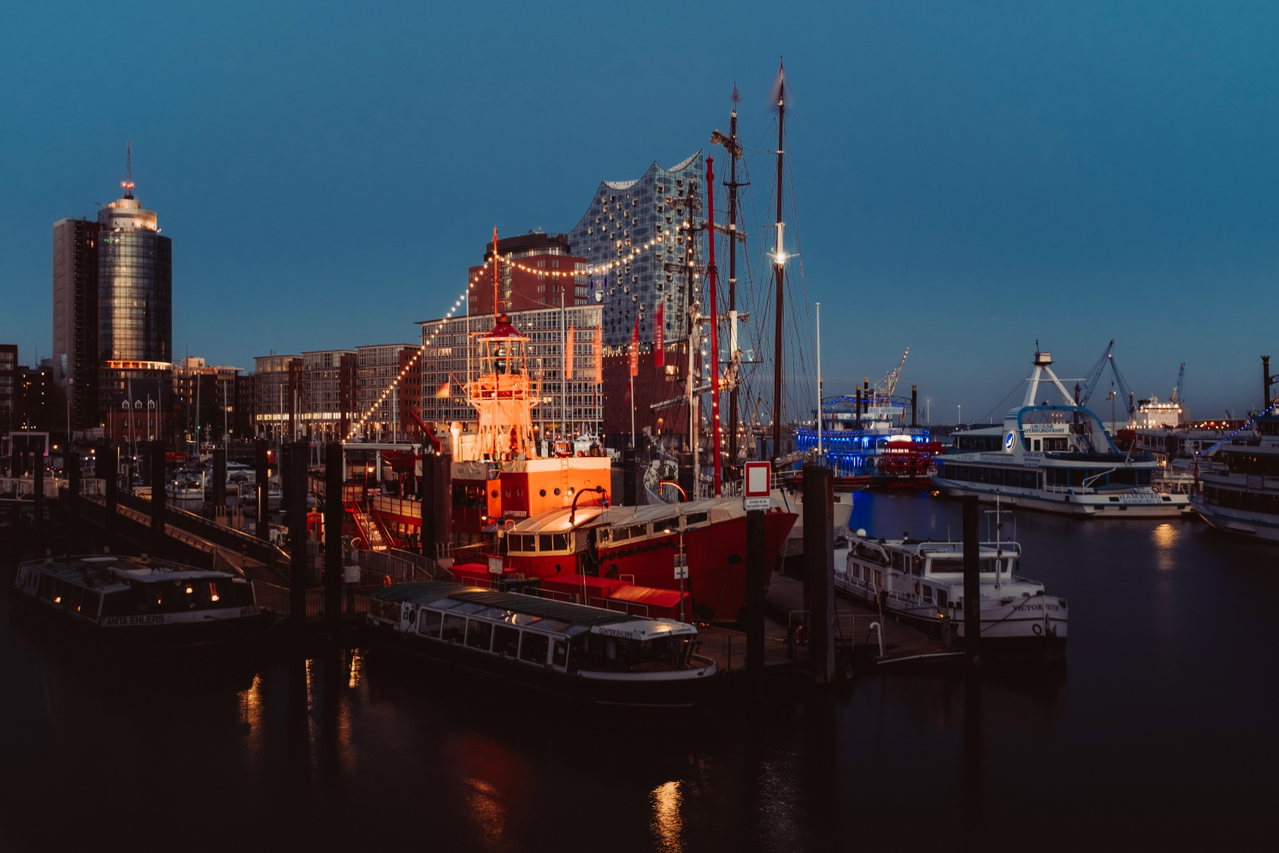 Historisches Segelschiff im Hamburger Hafen am Abend, dahinter beleuchtete Gebäude