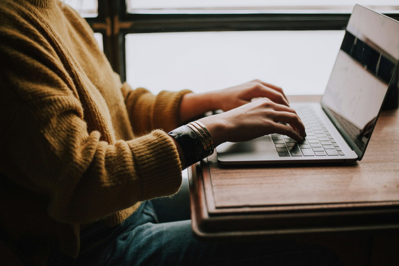 Person im Strickpullover arbeitet am Laptop vor einem Fenster