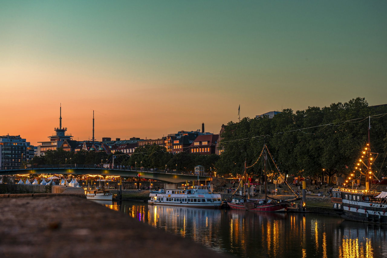Evening atmosphere on the Weser in Bremen, with illuminated ships along the promenade under an orange sky