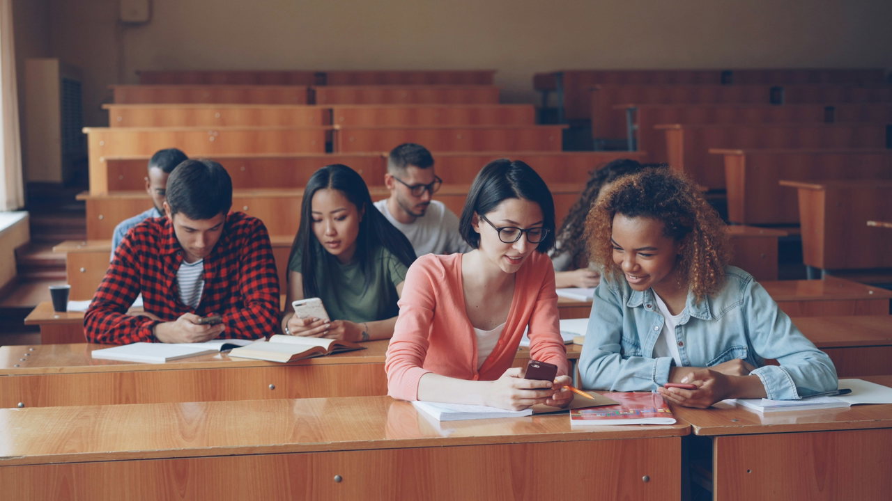 Studierende sitzen gemeinsam in den Bankreihen eines Hörsaals und schauen auf ihre Unterlagen.